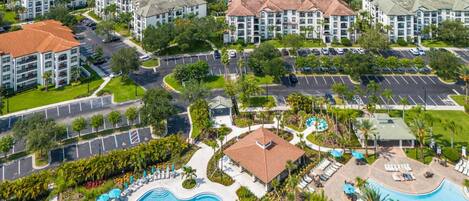 Un resort con varias edificaciones, una piscina grande y un lago al fondo.