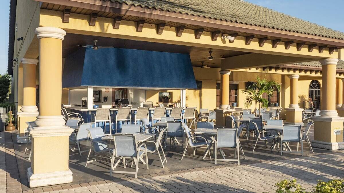 An outdoor patio with multiple tables and chairs, a covered seating area, and a building with columns and a tiled roof.