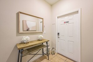 A hallway with a wooden console table, a mirror, a white door with a 'No Smoking' sign, and a small lantern. - Pp8968 - 4BR House With Pool Near Disney Parks (Kissimmee)