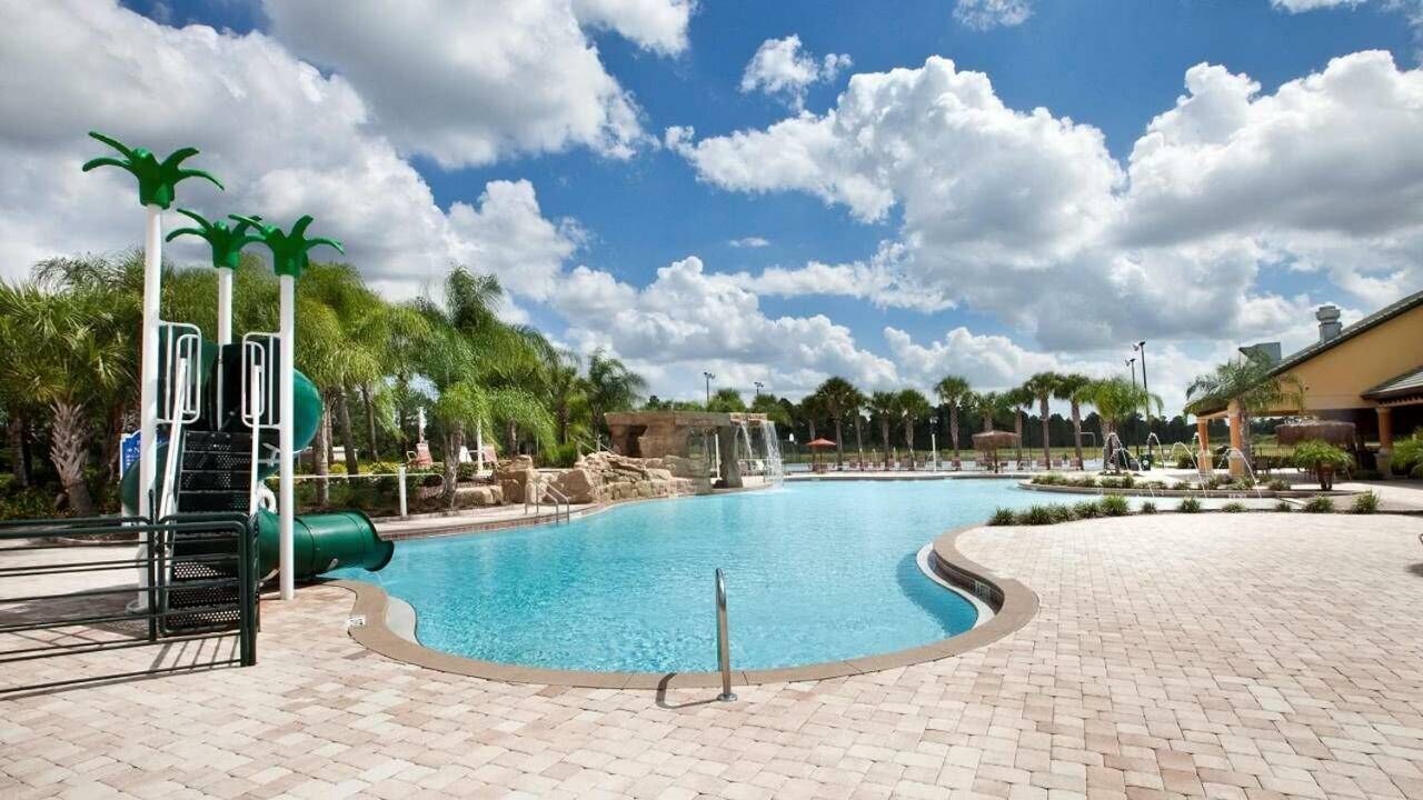 A swimming pool with a water slide, palm trees, and a brick patio.
