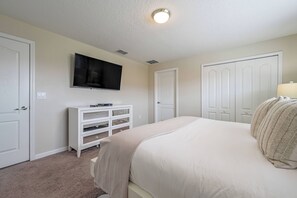 Ein Schlafzimmer mit Bett, Wandfernseher, Kommode und Kleiderschrank.