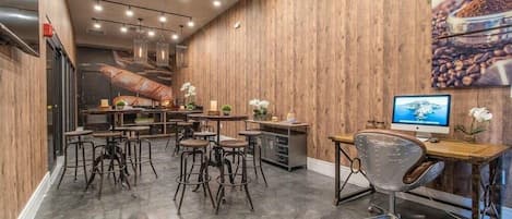 Interior de restaurante con paredes de madera, varias mesas y sillas, un escritorio con computadora y un televisor.