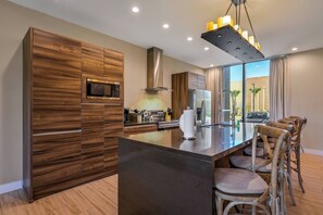 Une cuisine moderne avec des meubles en bois, un îlot central, des tabourets de bar et une vue sur l’extérieur.