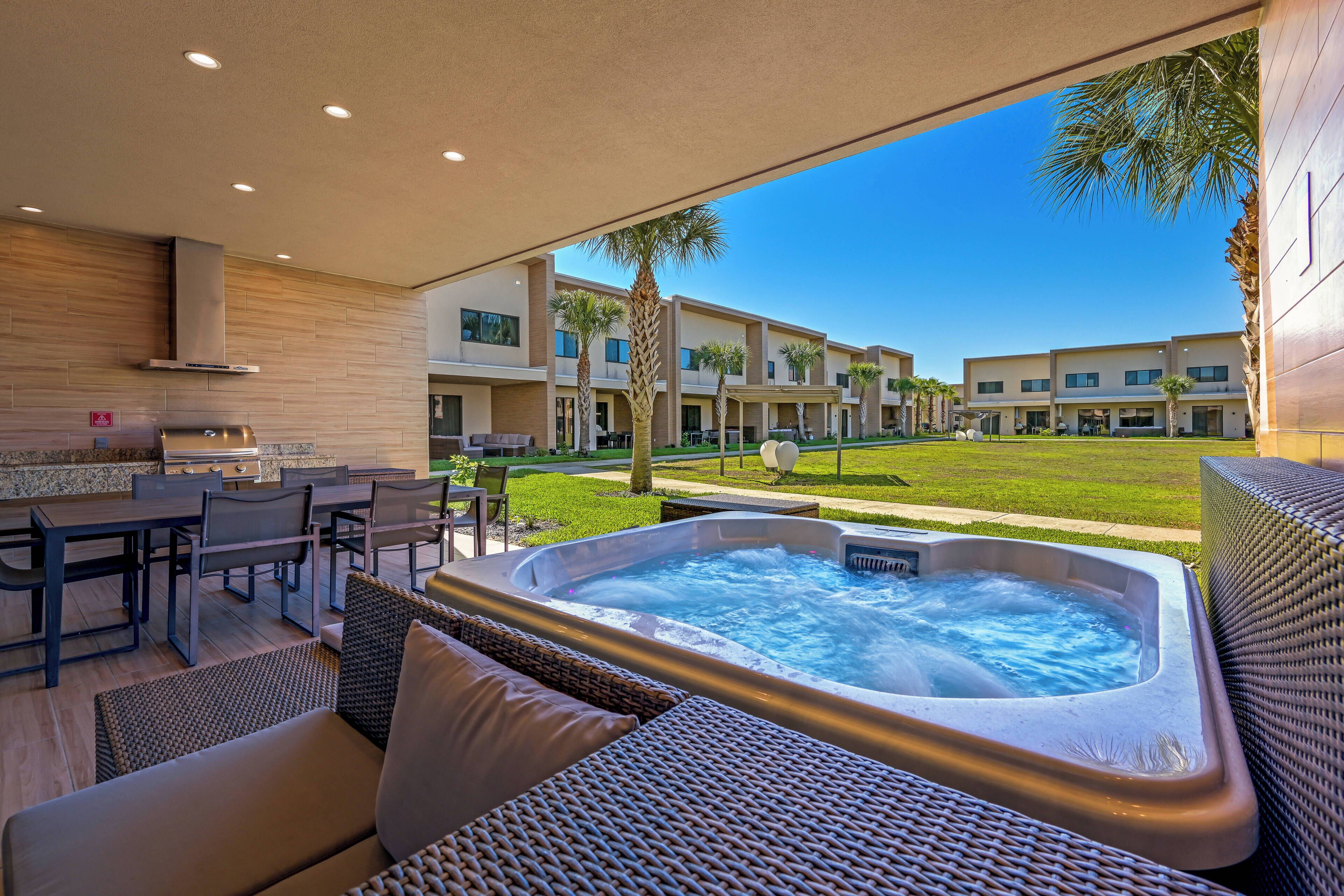 Un patio al aire libre con jacuzzi, mobiliario de mimbre y vistas a un conjunto de edificios.