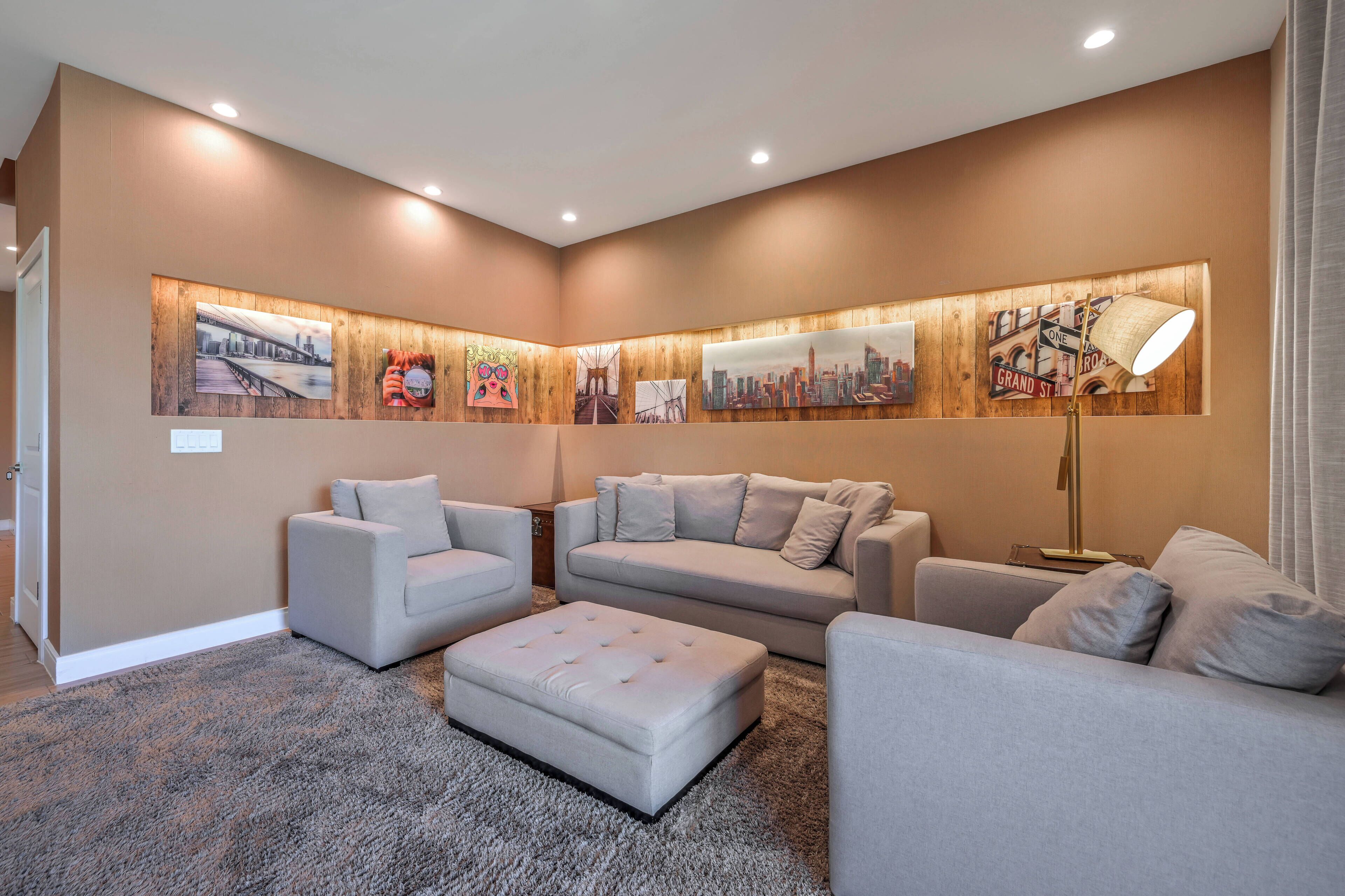 A modern living room with a sectional sofa, a loveseat, and an ottoman. The room features a large wooden accent wall with framed cityscape artwork.
