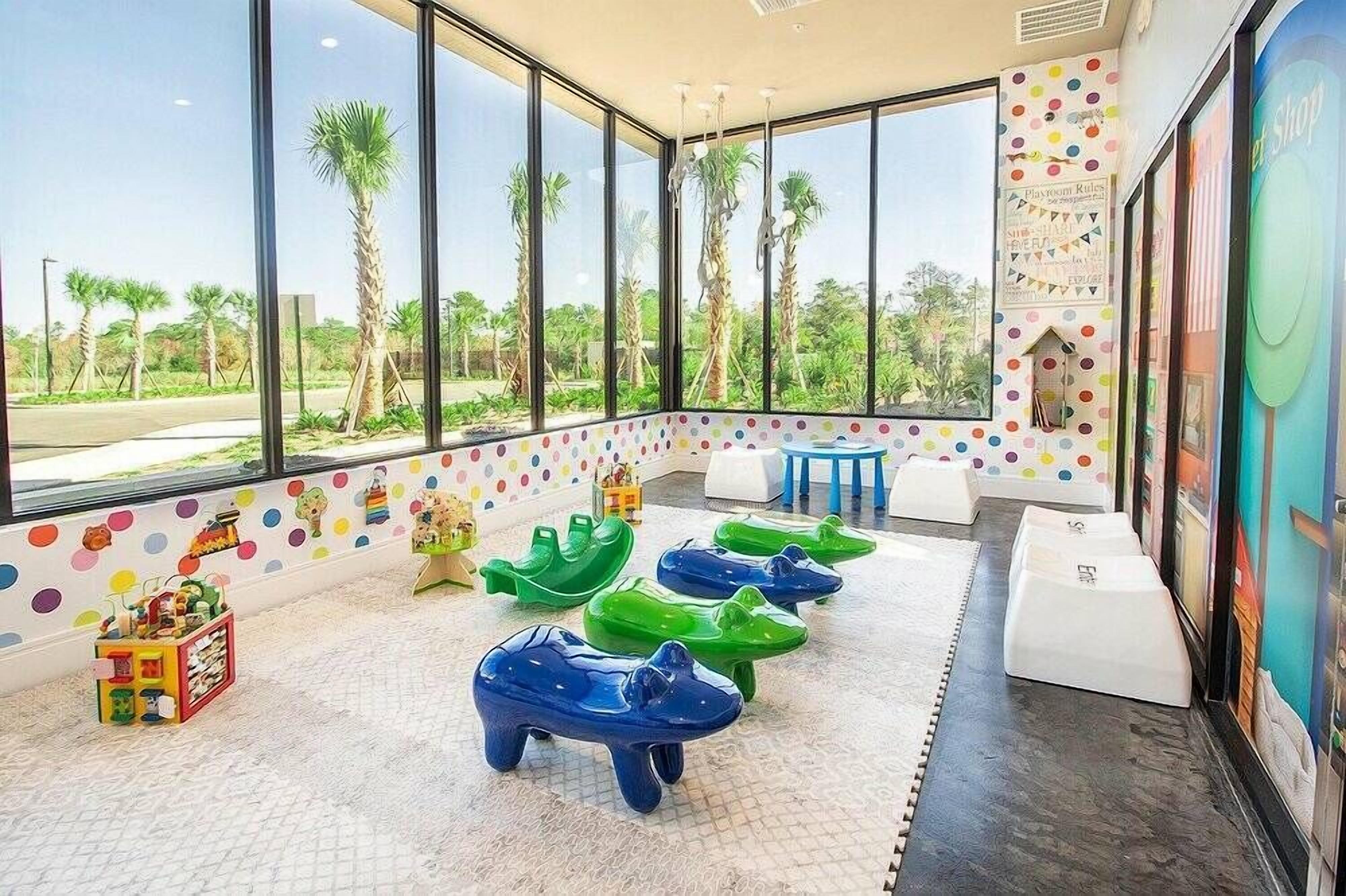 Zona de juegos infantiles con ventanas amplias, paredes de lunares coloridos y vistas a palmeras.