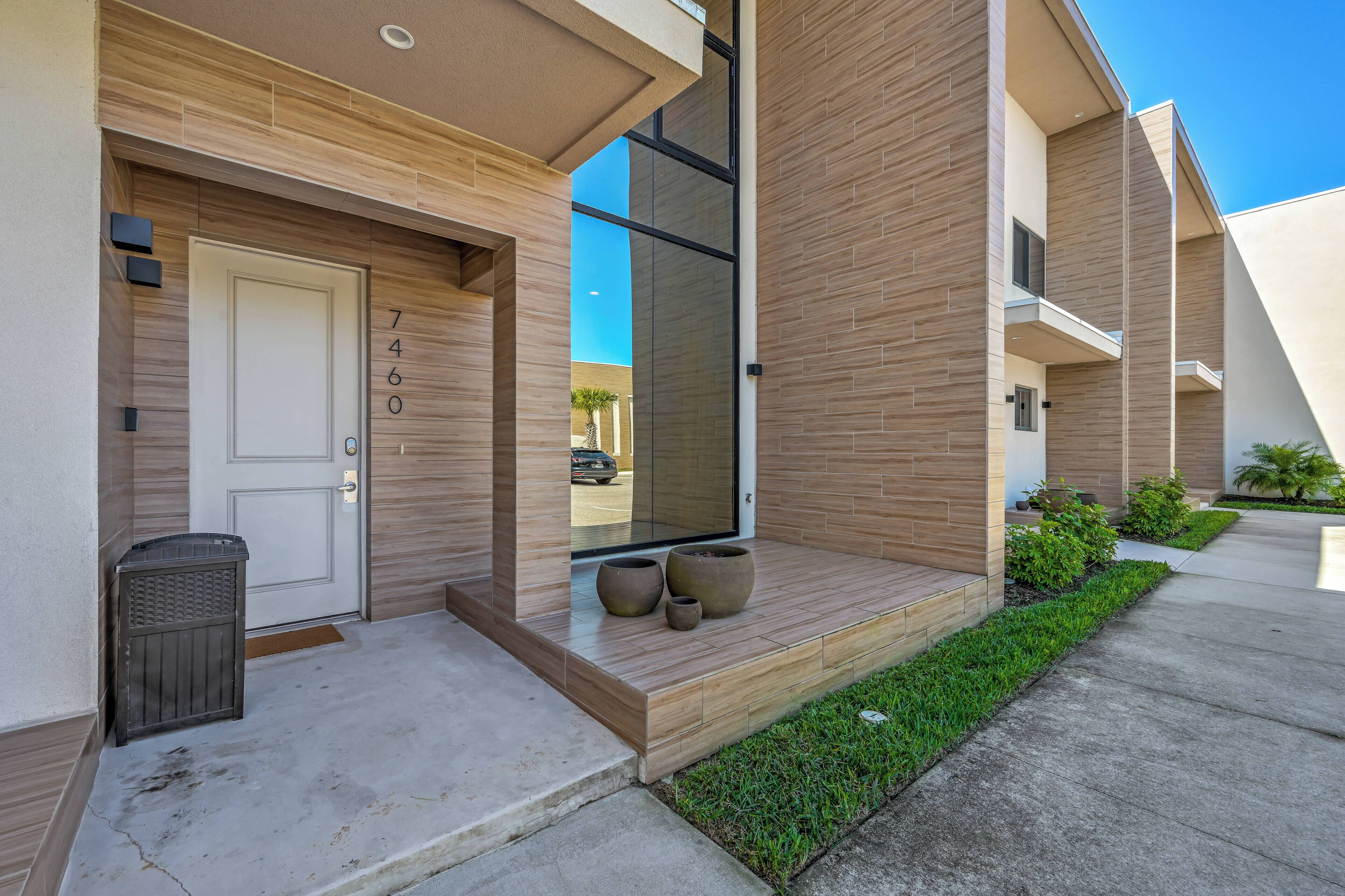 A modern building with a wooden facade, a door with a number, and a small garden area with potted plants.