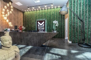 A reception area with a modern design, featuring a wooden reception desk, a green vertical garden wall, and a sign that reads "MAGIC VILLAGE Views". - Mvv7460 - 3BR House Near Disney w/ Hot tub (Kissimmee)