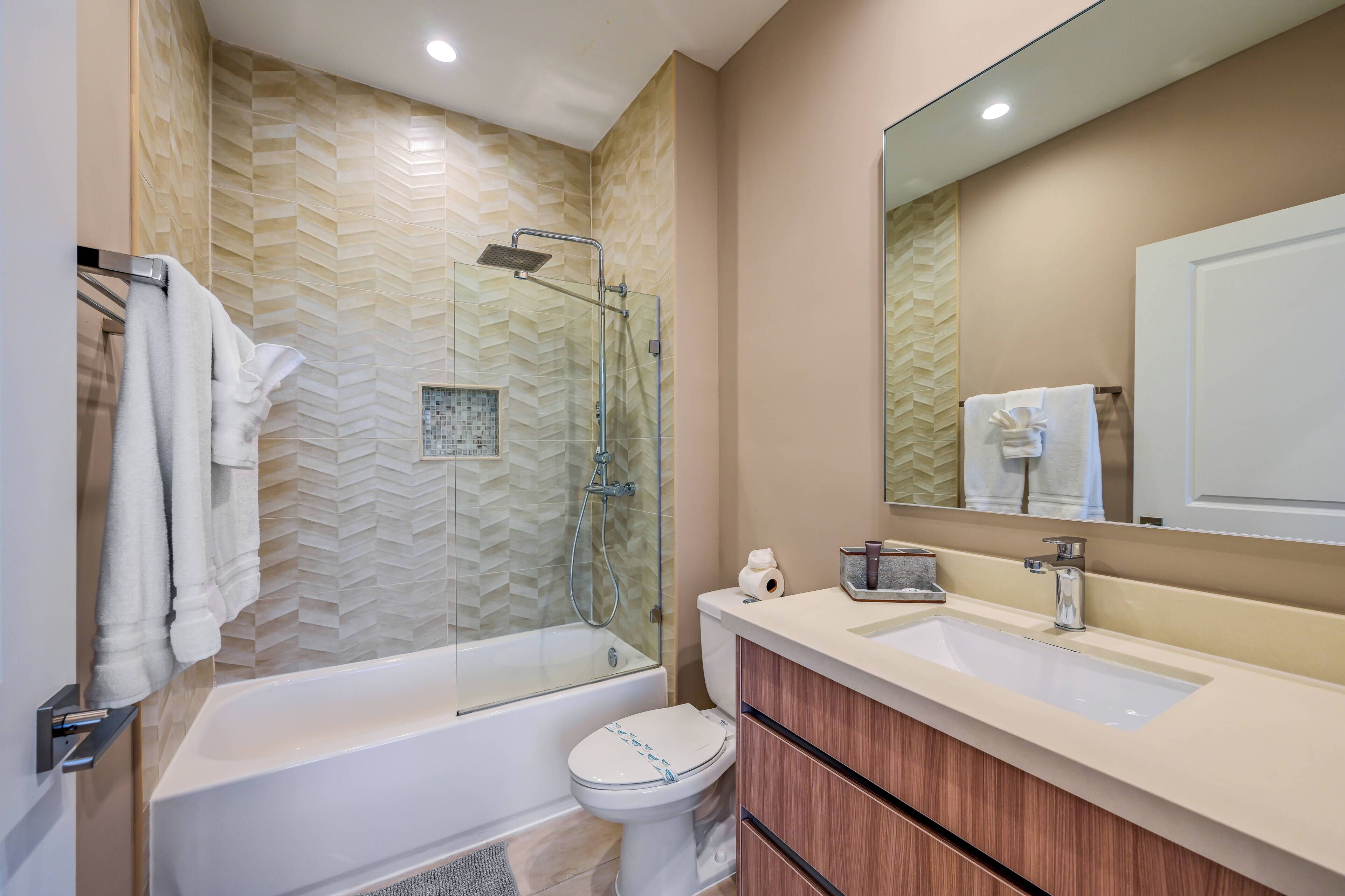 A modern bathroom with a glass-enclosed shower, a white bathtub, a toilet, and a vanity with a mirror.