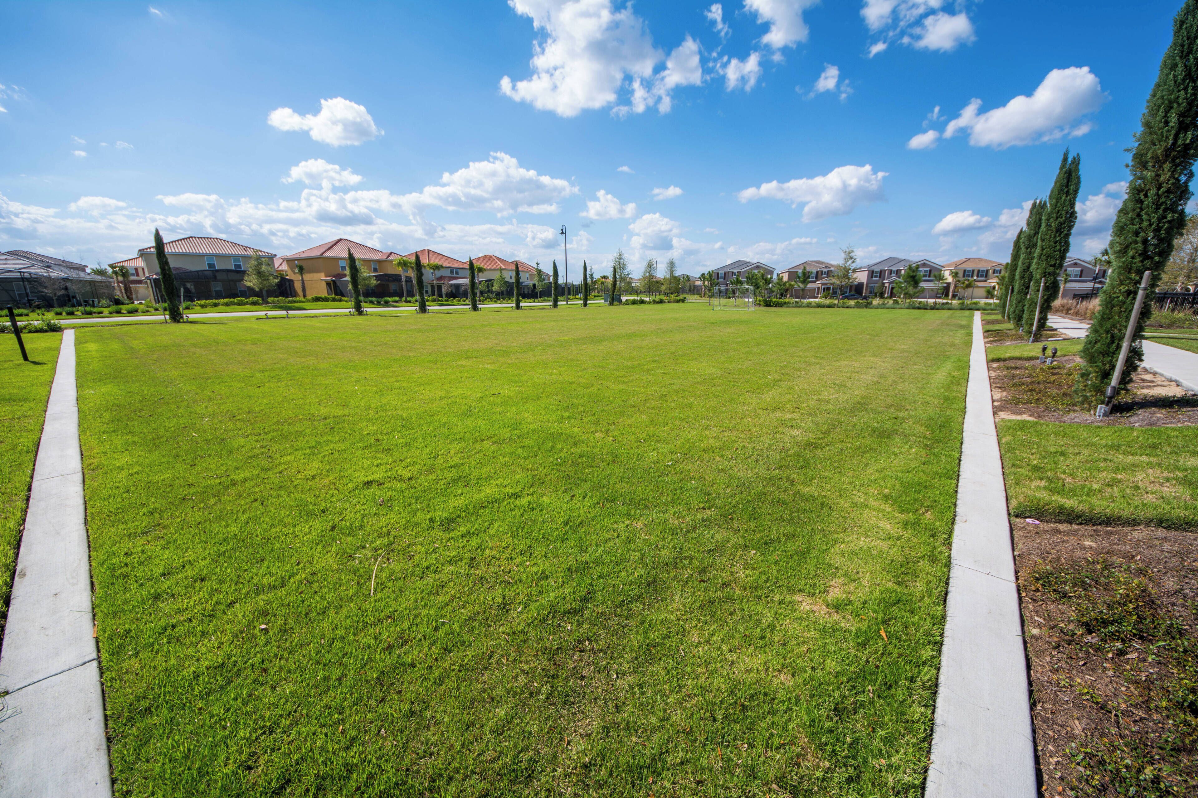 A well-maintained grassy area with a concrete path, surrounded by residential buildings and trees.