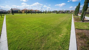 Een verzorgd gazon met een betonnen pad, omringd door woongebouwen en bomen.
