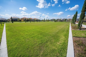A well-maintained grassy area with a concrete path, surrounded by residential buildings and trees. - St4344 - 7BR House With Pool Near Disney Area (Davenport)