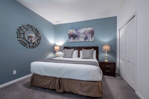 A bedroom with a bed, bedside lamps, a wall mirror, and a painting. - St4344 - 7BR House With Pool Near Disney Area (Davenport)