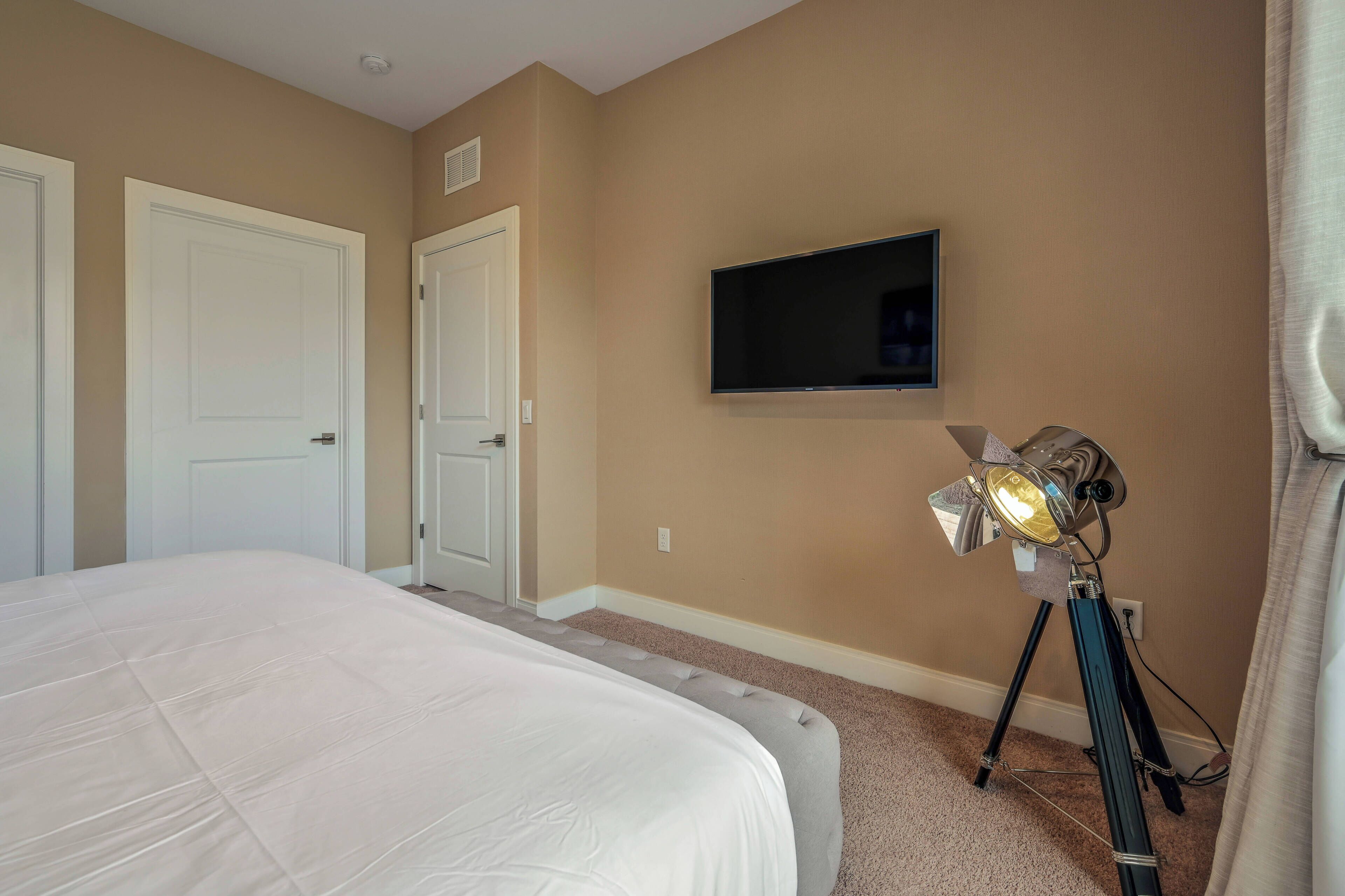 A bedroom with a bed, a mounted TV, and a tripod with a light.
