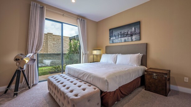 Ein Schlafzimmer mit einem großen Bett, einer Bank, einem Koffer, einer Lampe und einem Stadtbild.