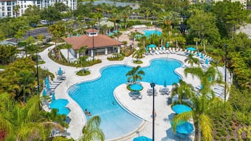 A resort with a large pool area, multiple lounge chairs, and a view of the surrounding cityscape.