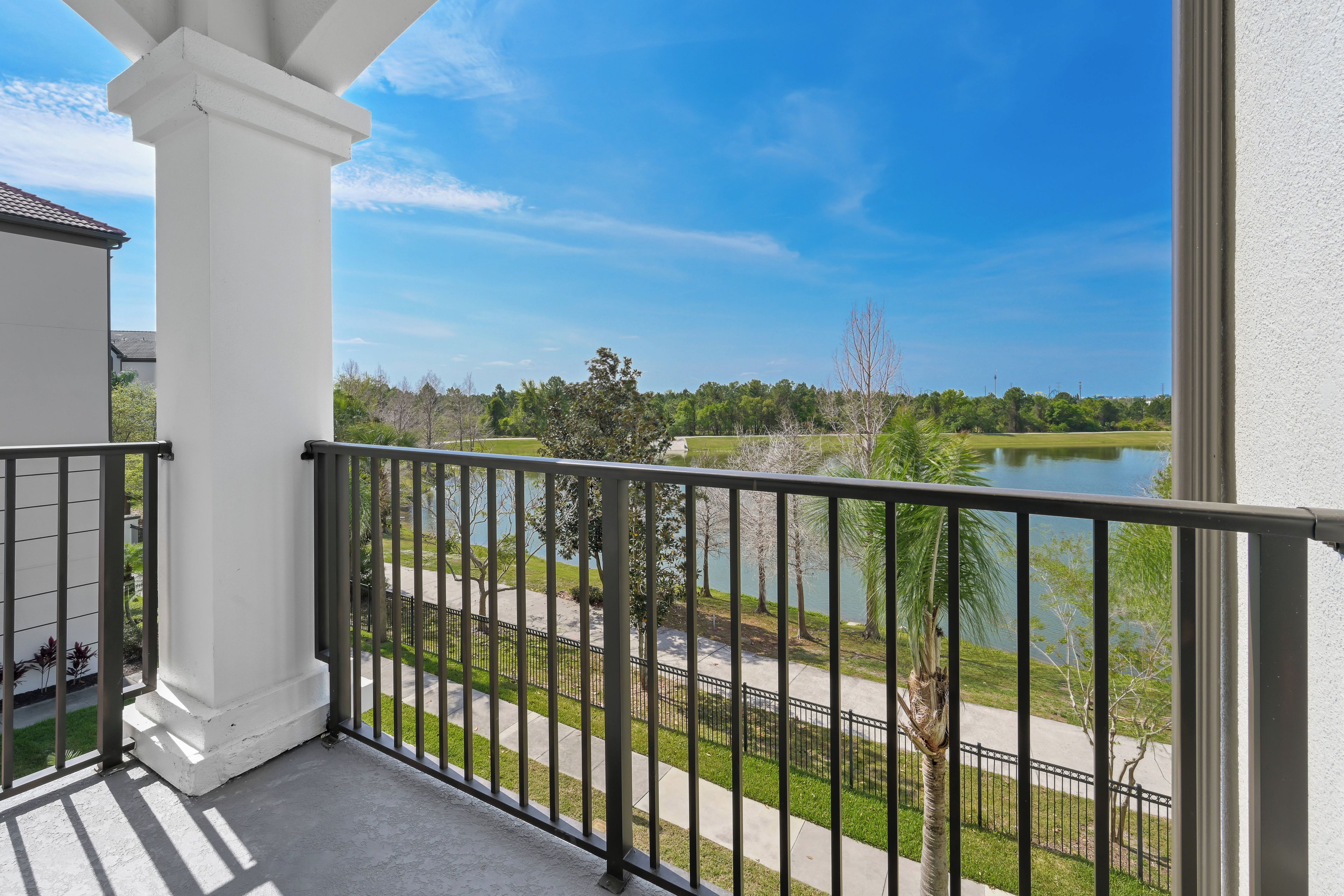 A balcony with a view of a lake, a white building, and a metal railing.