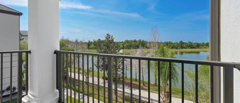 A balcony with a view of a lake, a white building, and a metal railing.