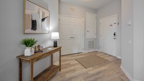 A hallway with a wooden console table, a potted plant, and a framed artwork. There are white double doors and a light fixture on the ceiling. - Is2-310 - 3BR Condo Near Disney and Universal (Orlando)