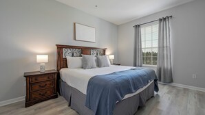 A bedroom with a bed, nightstands, a window with curtains, and a wall-mounted picture. - Is2-310 - 3BR Condo Near Disney and Universal (Orlando)