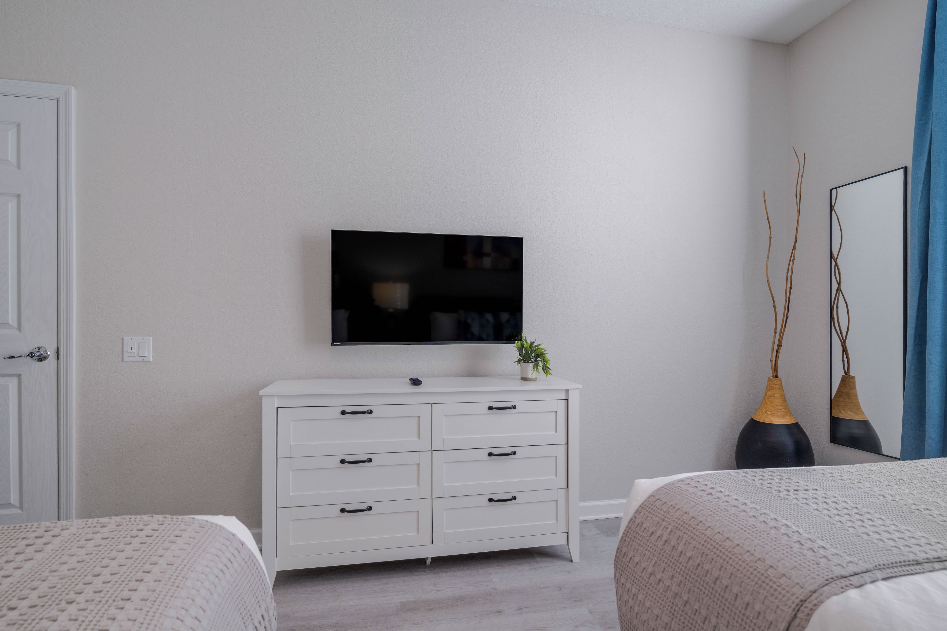 A bedroom with a white dresser, a flat-screen TV, two bedside tables, and a bed with a patterned bedspread.