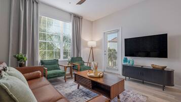A modern living room with a sofa, chairs, a coffee table, a TV, and a ceiling fan.