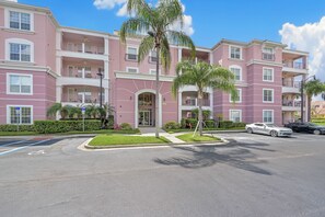 A multi-story pink building with balconies, a gated entrance, and a parking area with cars. - Vc10-208 - 3BR Large Condo Near the Attractions (Orlando)