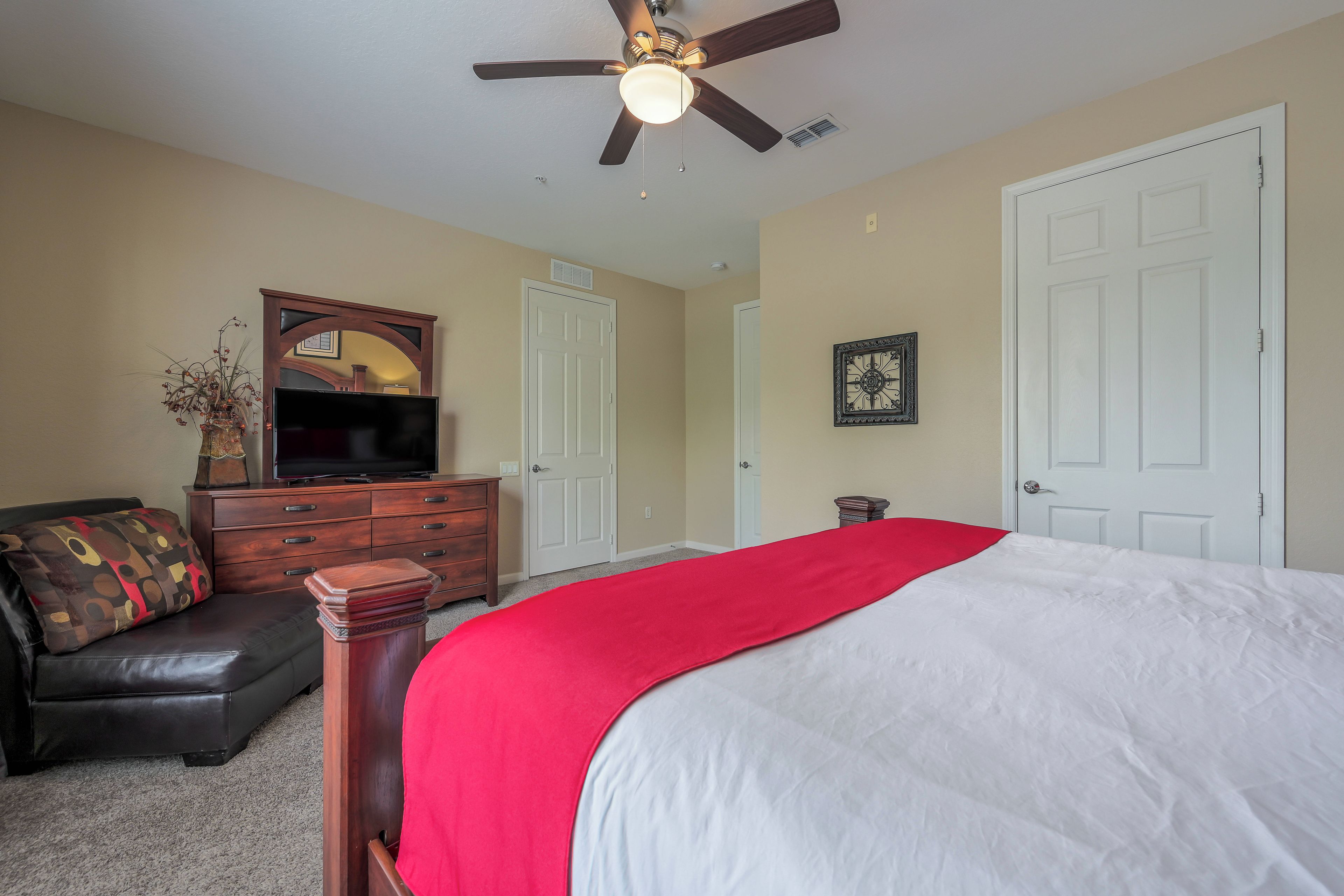 A bedroom with a bed, dresser, TV, and ceiling fan.