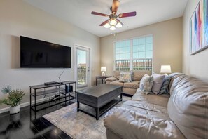 A modern living room with a flat-screen TV, a ceiling fan, a sofa, and a coffee table. - Vc8-410 - 3BR Condo With hot tub Near Disney (Orlando)