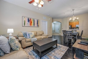 A living room with a sofa, coffee table, and a dining area with chairs and a table. - Vc8-410 - 3BR Condo With hot tub Near Disney (Orlando)
