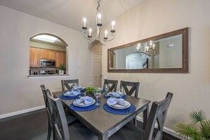 A dining room with a rectangular table set for six, surrounded by six chairs. A chandelier hangs from the ceiling, and a large mirror is mounted on the wall above the table. - Vc8-410 - 3BR Condo With hot tub Near Disney (Orlando)