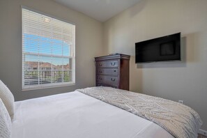 A bedroom with a bed, a dresser, a television mounted on the wall, and a window with blinds. - Vc8-410 - 3BR Condo With hot tub Near Disney (Orlando)