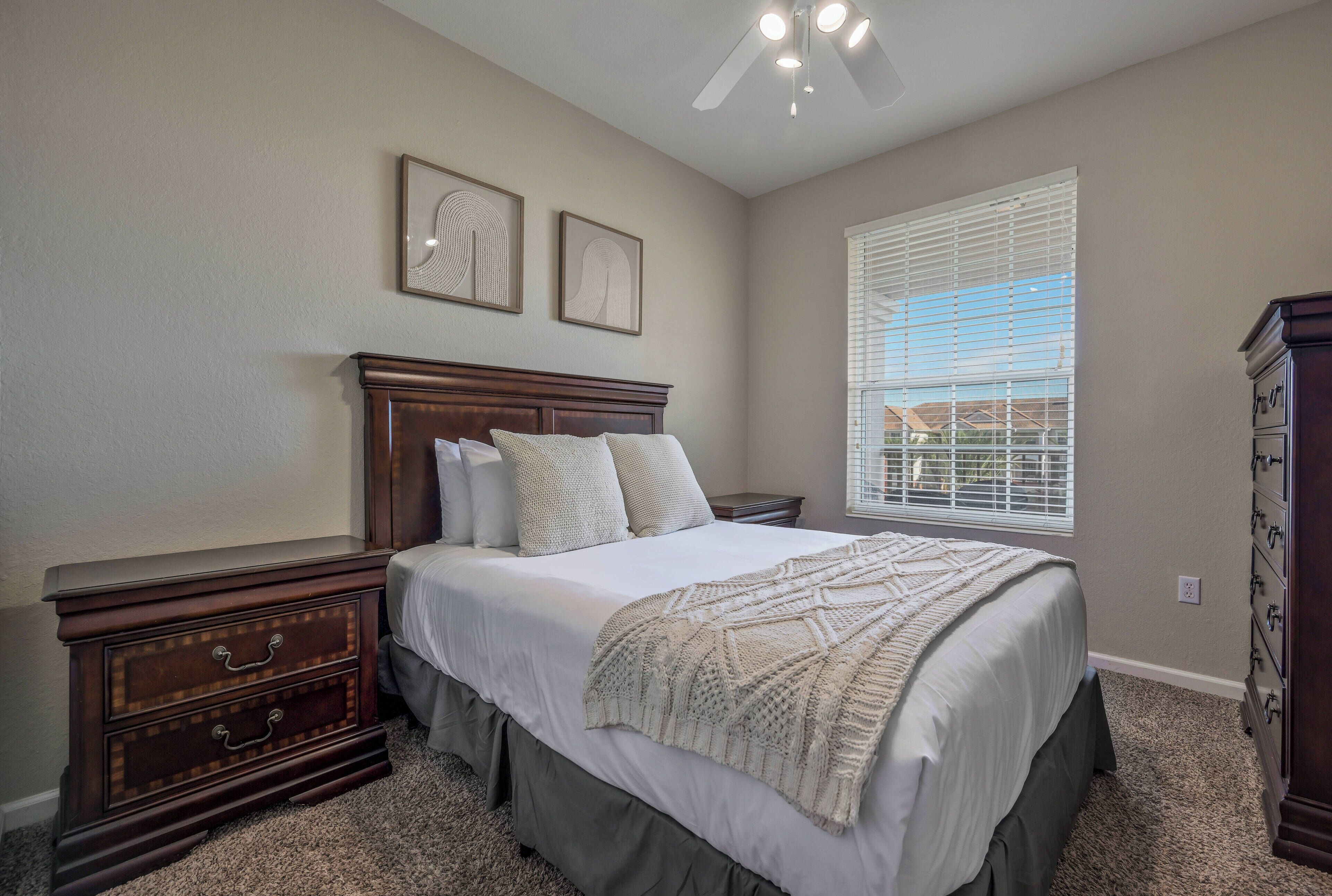 Une chambre à coucher comprenant un lit, des tables de chevet, une commode et un ventilateur de plafond.
