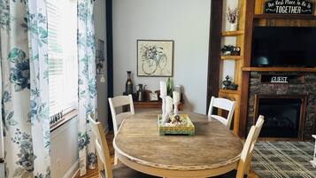 A dining area with a round wooden table, white chairs, a floral curtain, a fireplace, and a 'The Best Place To Be Is Together' sign.