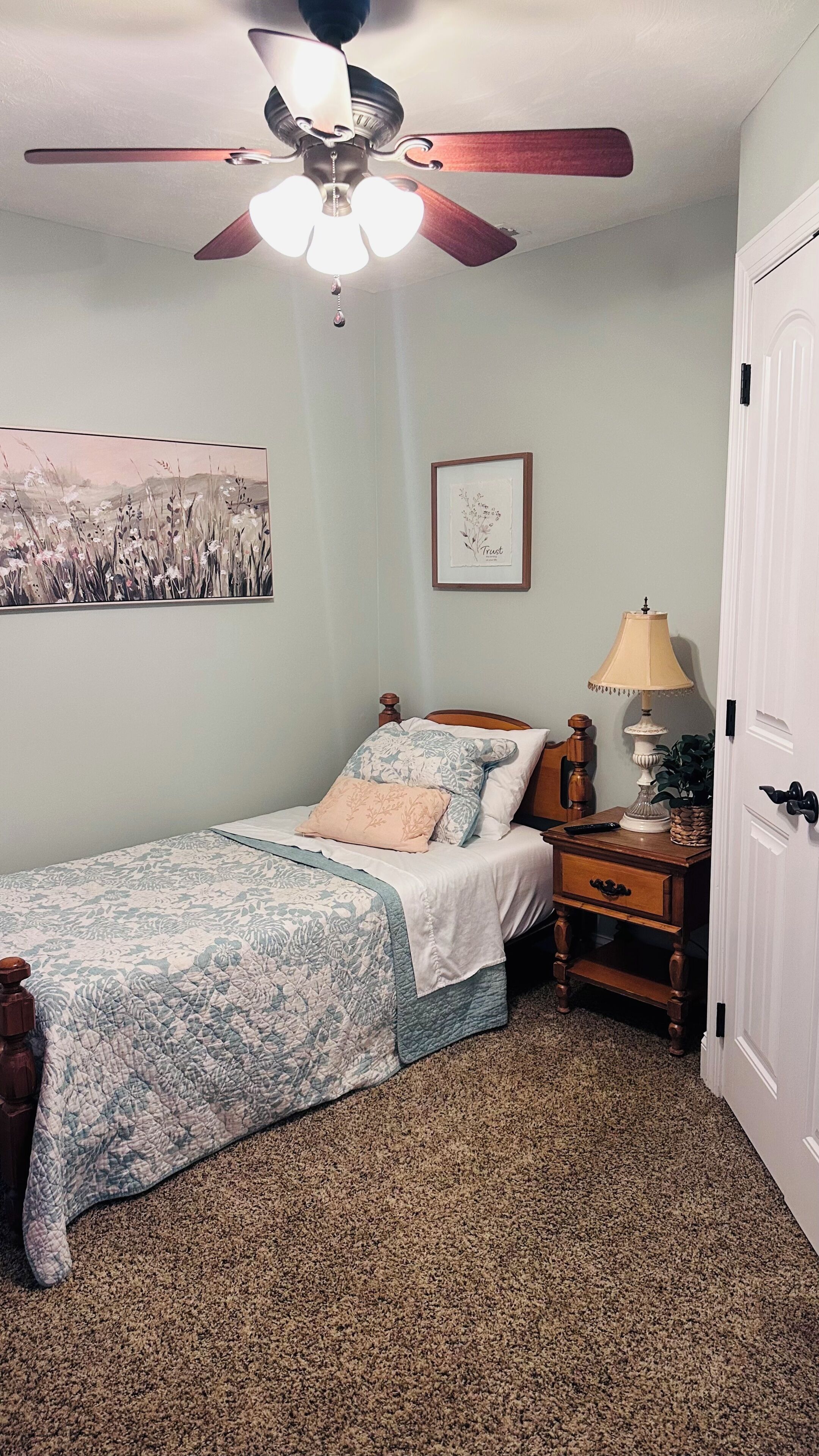 Une chambre à coucher avec un lit, une table de chevet, une lampe, un ventilateur de plafond et une porte.