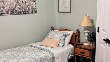 Une chambre à coucher avec un lit, une table de chevet, une lampe, un ventilateur de plafond et une porte.