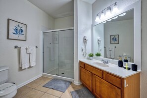 Een badkamer met een douchecabine van glas, een witte wastafel, houten kastjes en twee kunstwerken met bladeren in lijsten aan de muur.