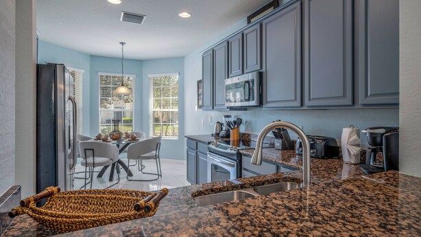 A modern kitchen with granite countertops, stainless steel appliances, and a dining area with a glass door to the outdoors. - Wh2545 - 5BR House Resort Access Near Disney Parks (Kissimmee)