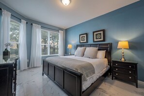 Ein Schlafzimmer mit einem Bett, zwei Nachttischen, einer Kommode und einem Fenster mit Vorhängen.