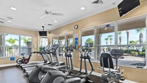 A gym with various cardio machines, large windows, and a ceiling fan. - Wh2545 - 5BR House Resort Access Near Disney Parks (Kissimmee)
