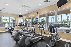 Ein Fitnessraum mit verschiedenen Cardiogeräten, großen Fenstern und einem Deckenventilator.
