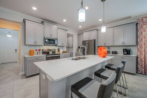 A modern kitchen with white cabinets, a large island with bar stools, and a microwave above the counter. - Cg9025 - 5BR House With Pool Near Disney (Davenport)