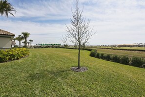 A well-maintained lawn with a single tree, a building with a green roof, and a clear sky. - Cg9025 - 5BR House With Pool Near Disney (Davenport)