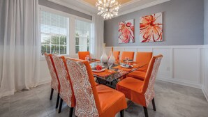 A dining area with a glass table, orange chairs, white curtains, and a chandelier. - Cg9025 - 5BR House With Pool Near Disney (Davenport)