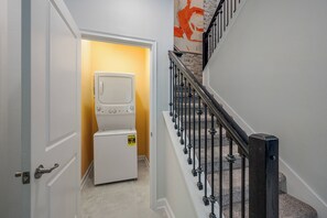 Ein Waschraum mit übereinander gestapelten Waschmaschinen und Trocknern, eine Treppe mit Metallgeländer und eine gelbe Wand.