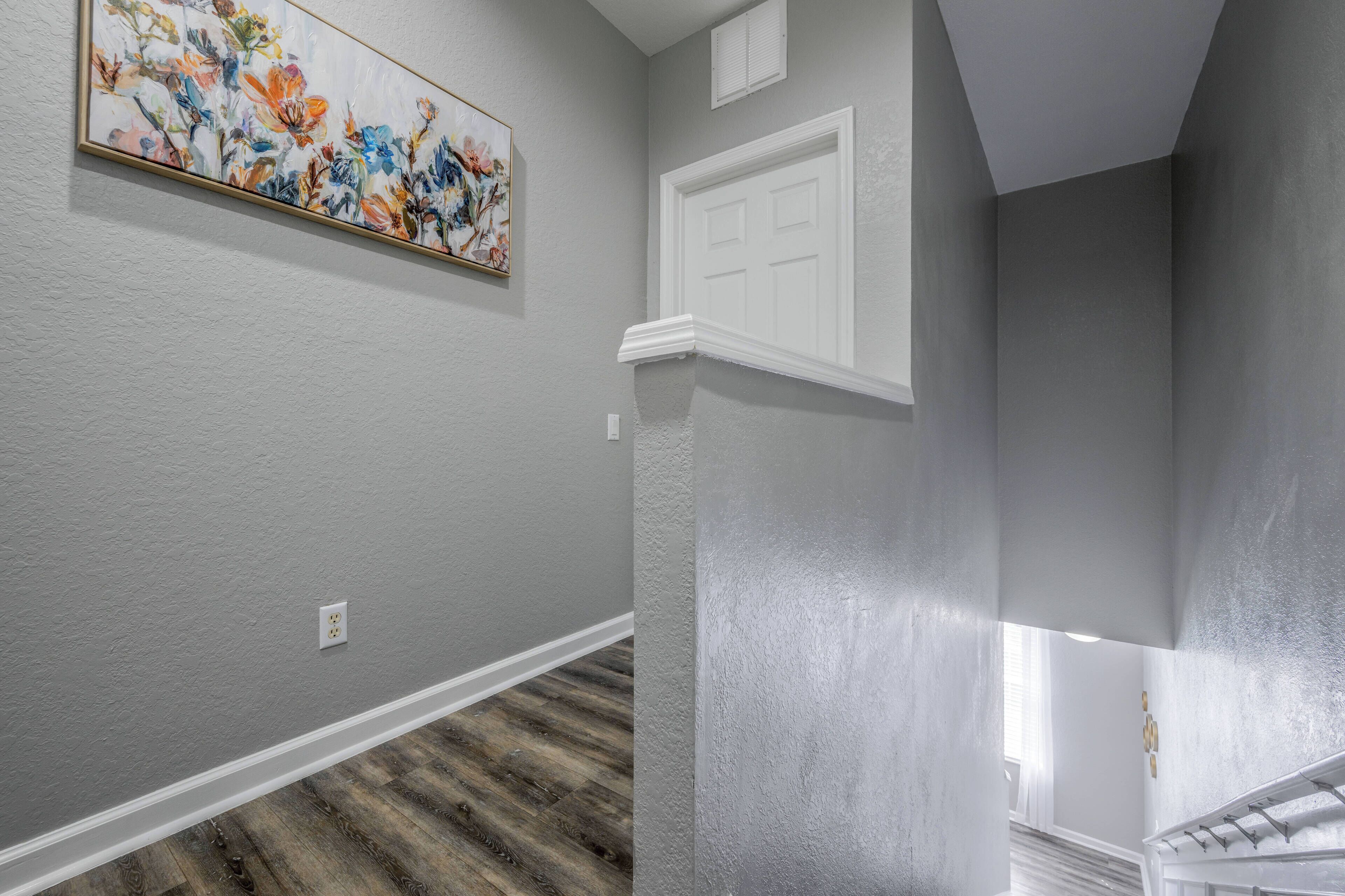 A hallway with gray walls, a wooden floor, a white door, and a painting on the wall.