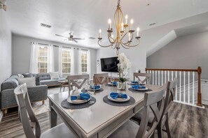 A dining area with a chandelier, a TV mounted on the wall, and a sofa in the background. - Th20 - 3BR House With Resort Access Near Parks (Orlando)