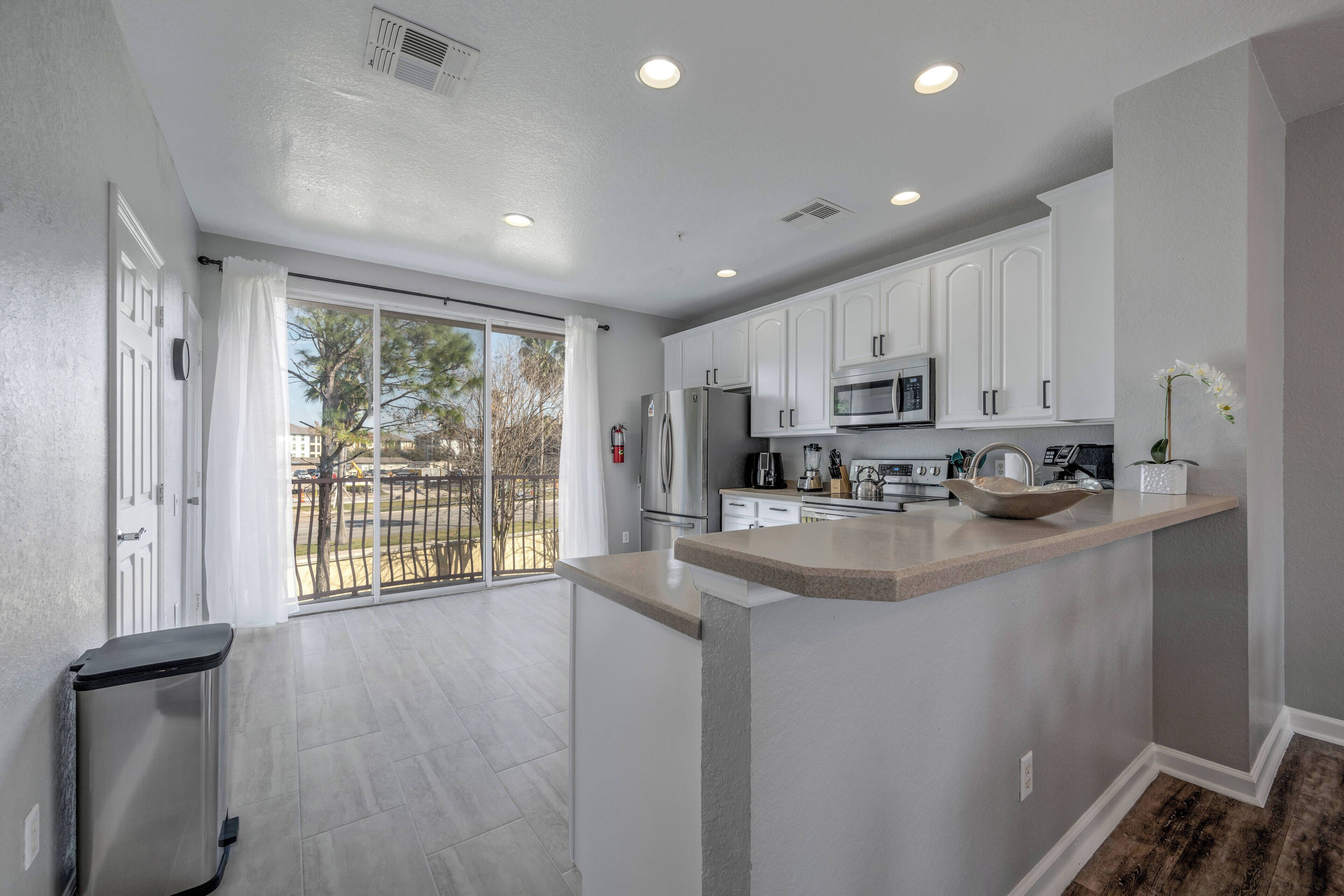A modern kitchen with white cabinets, a central island, and a sliding glass door leading to a balcony.