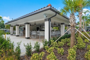 A covered outdoor seating area with tables and chairs, surrounded by palm trees and plants. - Th20 - 3BR House With Resort Access Near Parks (Orlando)