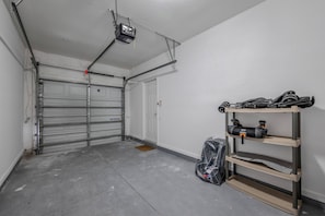 A garage with a closed garage door, a ceiling-mounted projector, and a shelf with tools. - Th20 - 3BR House With Resort Access Near Parks (Orlando)